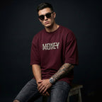 Man wearing a maroon t-shirt with 'MONEY' text, sitting on a stool against a dark background